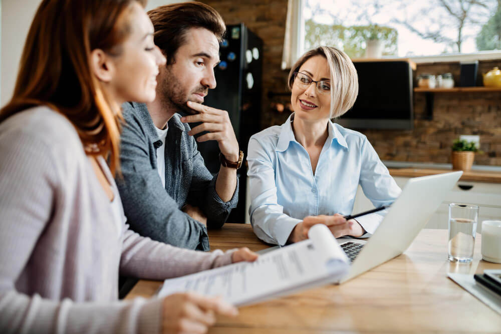 smiling financial advisor using laptop while having meeting with young couple (1)